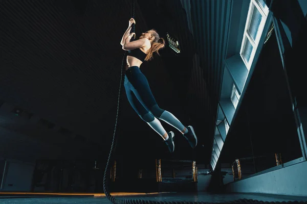 Full length wide angle shot of a woman performing rope climbs at