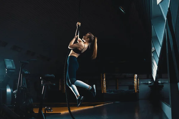 Full length wide angle shot of a woman performing rope climbs at