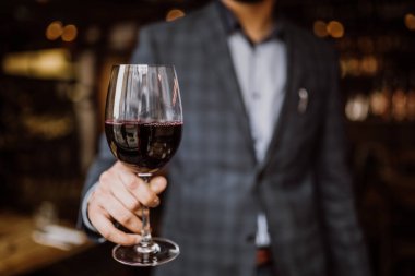 Mavi elbiseli bir genç adam bir kadeh kırmızı şarap tutuyor. Restoran, misafirperverlik ve içecek konsepti.