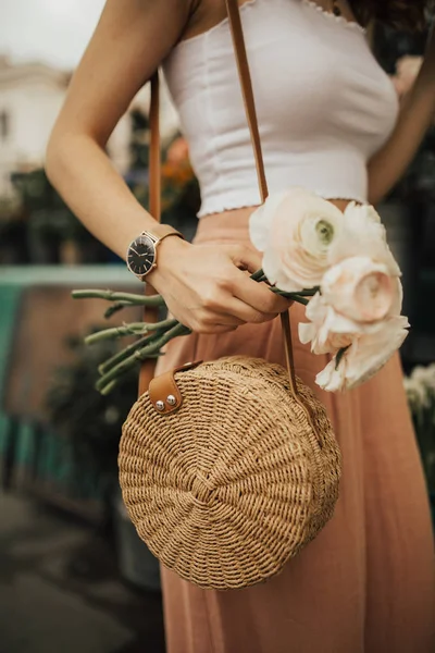 Çiçek pazarında çiçek bir demet tutan moda genç blogger kız. Bloglama ve sokak stili moda kavramı. Yaz ve bahar kıyafet fikirleri.