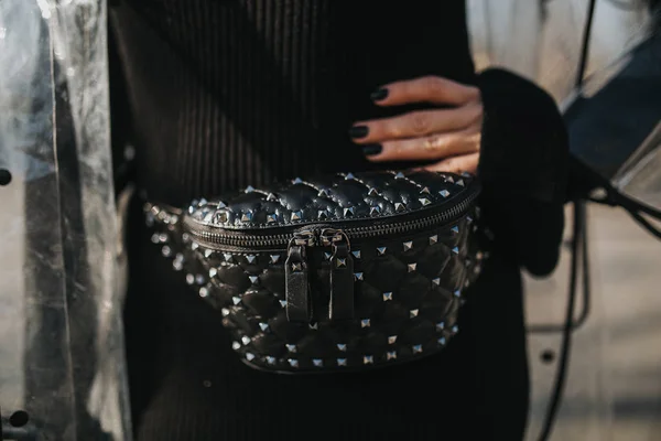 Young fashionable girl wearing a waterproof, transparent raincoat on top of the long black dress. Close up shot of outfit's details. Selective focus on the belt bag on the hip. Concept of blogging, fashion and accessories.
