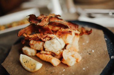 Kahverengi yağlı kağıt üzerinde sebze ile derin kızarmış deniz ürünleri tabağı bir yakın çekim. Yemek, catering ve restoran konsepti.