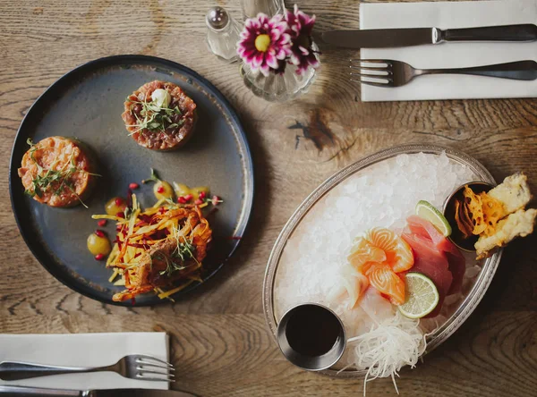 Soya sosu, ton balığı ve havuç salatası ile somon tartar ile sashimi tabağı düz bir atış yatıyordu. Catering, restoran ve çiğ gıda kavramı. Üst görünüm, plakalar üzerinde seçici odak. Tam olarak yemek masası kurmak.