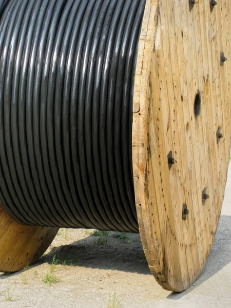 Black electrical wires in plastic coating on wooden spool, reparation works, construction materials.