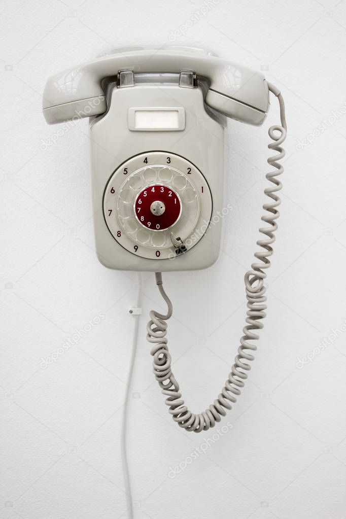 Old fashioned gray rotary telephone hanging on white wall. Vertical photo.