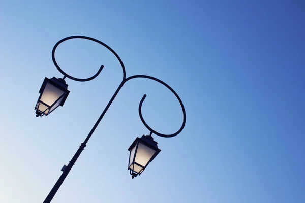 Beautiful vintage street lamp in a park on the clear blue sky background located in the left image side.