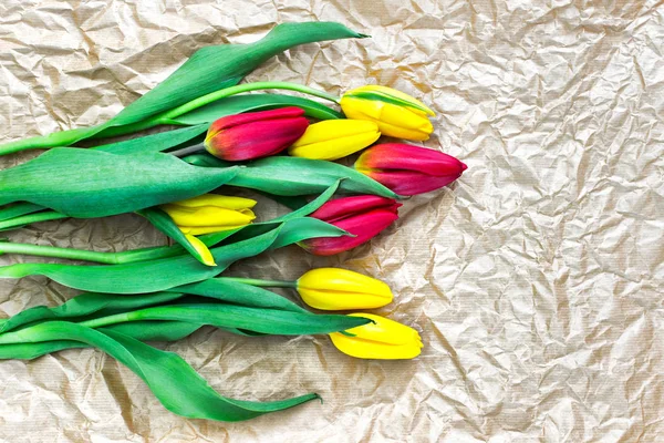 Bouquet of red and yellow tulips laying on wrinkled craft paper with blank space for text.