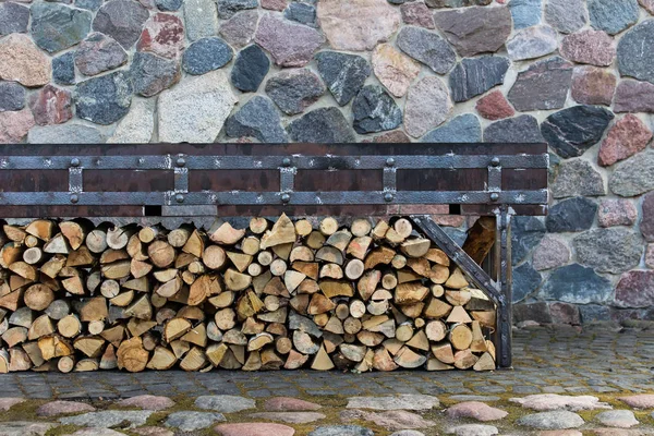 Neatly arranged wood logs under the fireplace on the background with ancient stone wall.