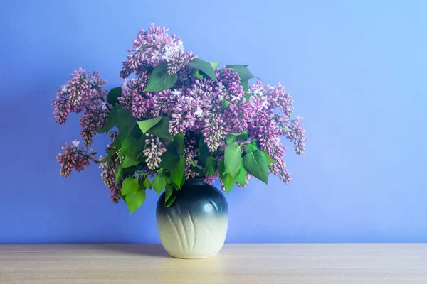 Bouquet of lilac flowers in a vase on blue background. Romantic summer syringa flowers.