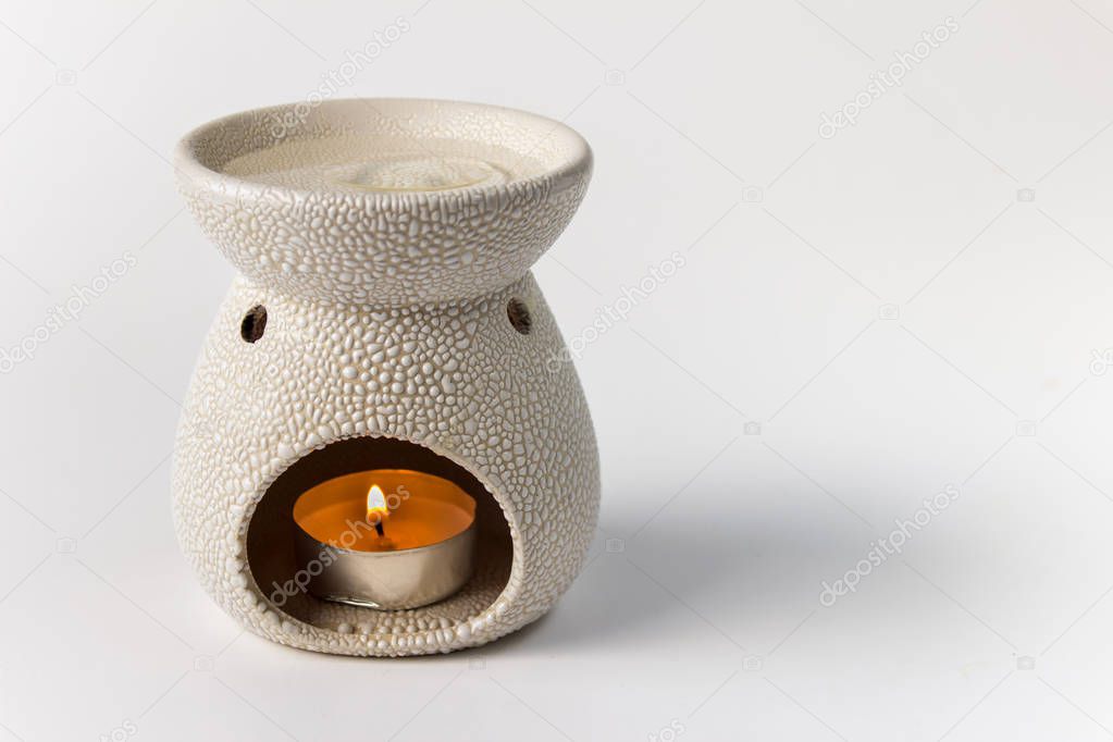 Aroma lamp with burning candle and water with drop of aroma oil on white background with blank space. Aromatherapy accessories.