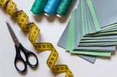 Zelené a modré barevné šití látkových vzorků s měřicí páska, nůžky a modrá a zelená vlákna na bílém pozadí.
