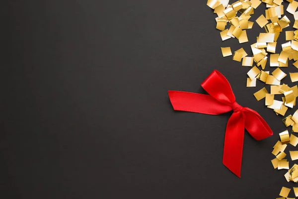 Red gift bow with golden confetti on black backgound — ストック写真