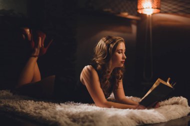 Bookshelf bir kitap okuma altında bir halı üzerinde siyah seksi vücut içinde yatan uzun kahverengi saçlı Glamour kadın tarafından floot lamba yaktı