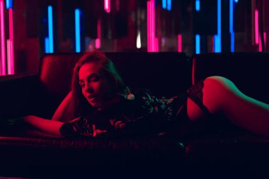 Seksi genç kadın yatakta neon ışıkları bir duvara dışarı bükülmüş yalan