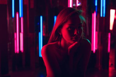 Oturan güzel genç kadın portresi elini neon ışıkları bir duvara yaslanmış