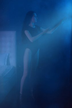 Çekici genç kadın güzel bir siyah tüyleri ve çıplak uzun bacaklı seksi siyah iç çamaşırı mavi Ay'da arıyorsunuz bir cadı kostümü olarak ışık ellerinin üzerinde düşen ve parmaklarını yalak akan.