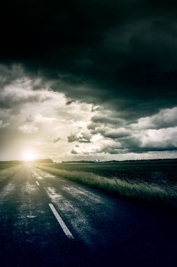 Ufukta dramatik bulutlar olan asfalt yol