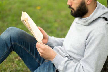 Parktaki çimlerde kitap okuyan bir adam.