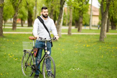 Parkta bisikleti olan sıradan giysili genç yakışıklı bir adam.