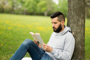 Genç adam parkta kitap okuyor.