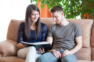 Genç çift evdeki kanepede kitap okuyor.