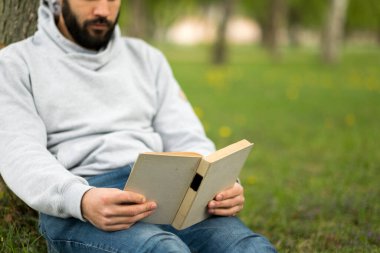 Genç adam parkta kitap okuyor.