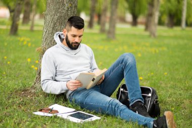 Genç adam çimenlerde oturup kitap okuyor.