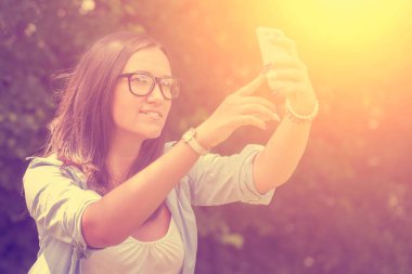 Genç bir kadın parkta akıllı telefonuyla selfie çekiyor.
