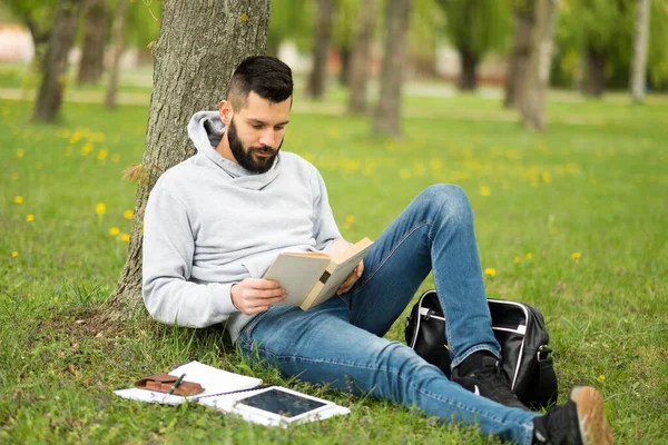 Genç adam çimenlerde oturup kitap okuyor.