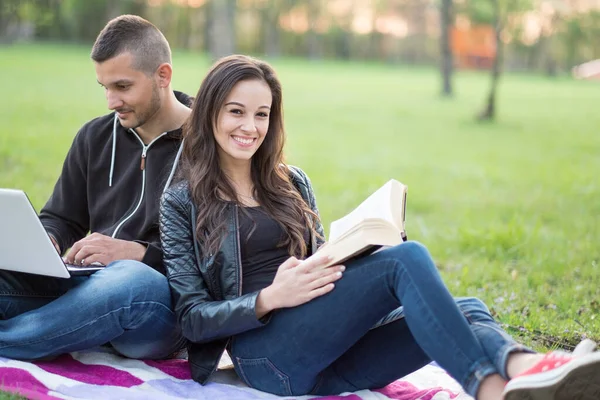 young couple in the park with laptop and book