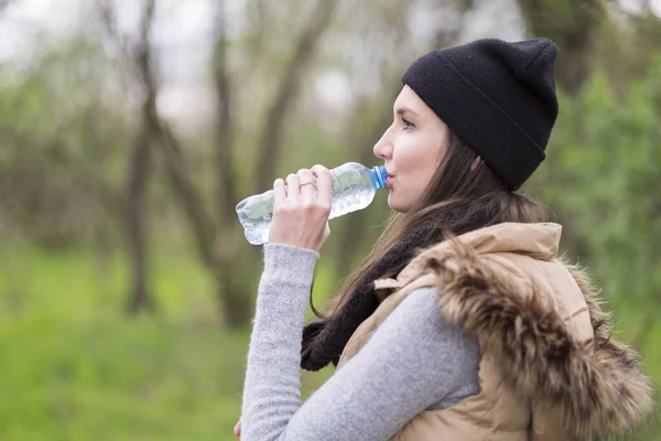 寒い気候の瓶から水を飲む若い女性は ロイヤリティフリーのストック画像