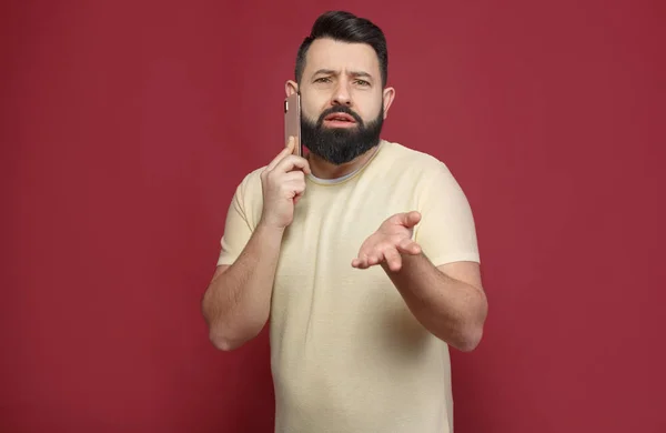 Şirin ve sakallı bir esmer adam kırmızı bir arka plan üzerinde duygusal telefonda diyor