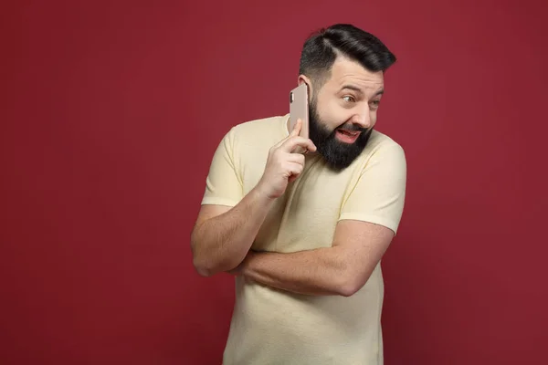 Şirin ve sakallı bir esmer adam kırmızı bir arka plan üzerinde duygusal telefonda diyor