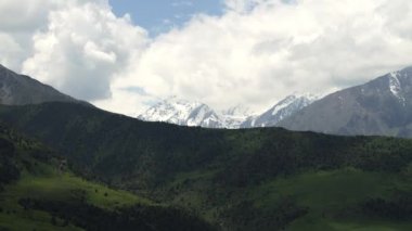 Kümülüs bulutları dağın tepelerinde hareket eder, dağların yeşil yamaçlarında gölgeler dökülür, zaman atlamalı, Tien Shan dağlarında güneşli gün, Kırgızistan