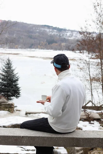 Man has coffee in winter time in fresh air and looks at the frozen lake