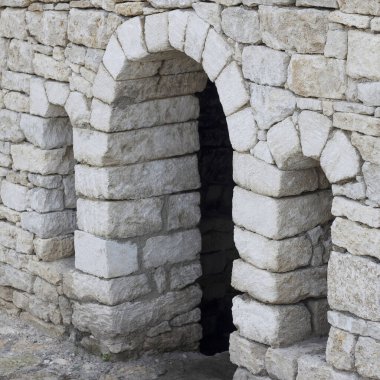 Kaba yontulmuş bloklardan yapılmış eski bir taş kemer yolu. Yapıda yıpranma ve yaşlanma belirtileri var. Tarafsız bir arkaplanda geçiyor.