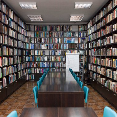 CHISINAU, MOLDOVA - 14 Mart 2025; Uzun ahşap masalar, mavi sandalyeler ve seramik zemindeki kitaplarla dolu kütüphane iç mimarisi, eğitimi ve bilgiyi simgeliyor