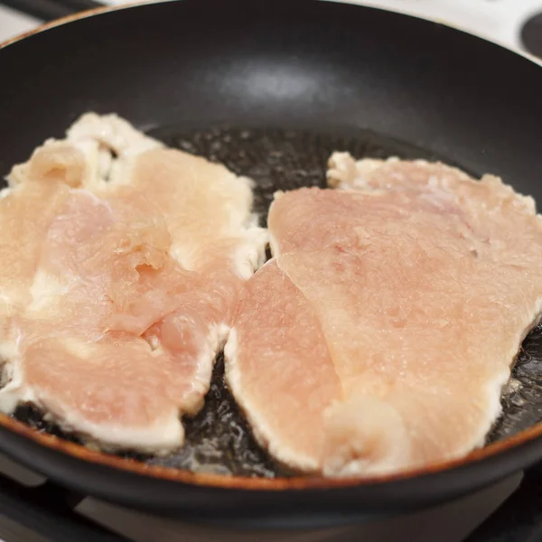 Kızartma tavasında pişen et tavuğu dilimleri. Et açık pembe tavada eşit olarak dizilmiştir. Geçmişi bulanık, yiyeceğe odaklanmış.