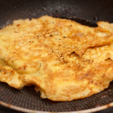 Yumurta hamurunda bir parça et kızartma tavasında kızartılır. Kızarmış sarı yumurta hamurunda et, iştah açıcı ve tavaya eşit olarak yerleştirilmiş, yakın plan.