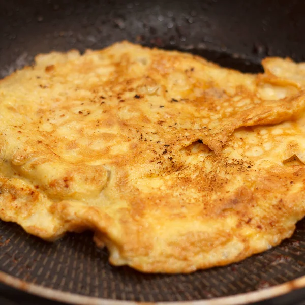 Yumurta hamurunda bir parça et kızartma tavasında kızartılır. Kızarmış sarı yumurta hamurunda et, iştah açıcı ve tavaya eşit olarak yerleştirilmiş, yakın plan.