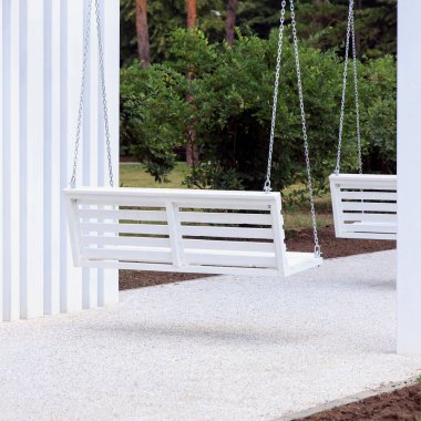 Minimalist bir yapının altında beyaz salıncakların olduğu modern bir açık hava alanı. Bölge yeşilliklerle çevrili, sakin bir ortam yaratıyor.