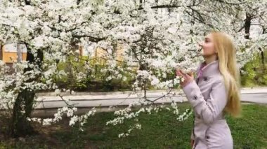 Güzellik genç kadın bahardoğa zevk , Çiçek açan ağaçları ile Bahçe Happy Beautiful kız. El gimbal tarafından yavaş çekim video çekimi
