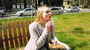 Sokakta oynayan genç bir kız kameraya baloncuk üflüyor. Ağır çekim. Güzel kız bahar, yaz ve baharda parkta sabun köpüğü üflüyor ve gülümsüyor..