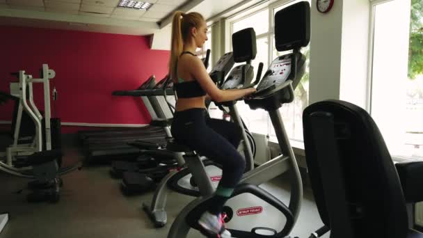 在运动健身房里骑着健身自行车的漂亮女孩 — 图库视频影像