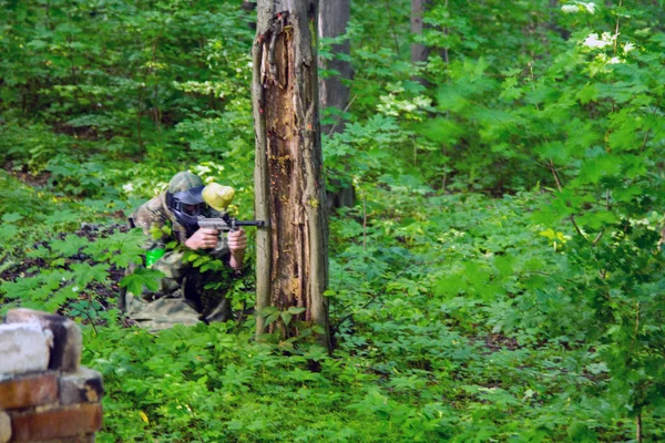 Paintball jugador deportivo con máscara protectora apuntando arma y derribado con salpicaduras de pintura en verano — Foto de Stock