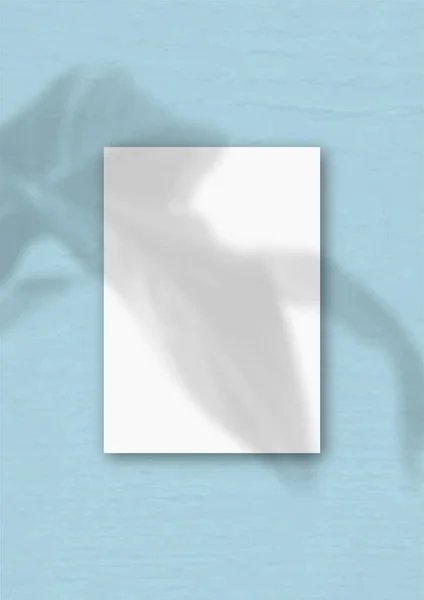 A folha vertical de papel A4 texturizado branco no fundo da parede azul. Mockup se sobrepõe às sombras das plantas. A luz natural lança sombras de uma fábrica exótica — Fotografia de Stock