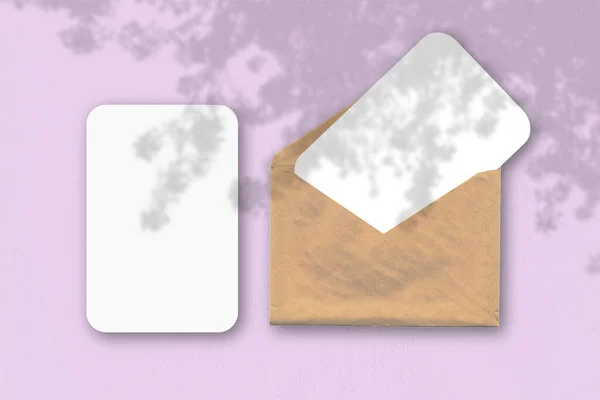 An envelope with two sheets of textured white paper on a pink table background. Mockup with an overlay of plant shadows. Natural light casts shadows from a tropical plant. — Stock Photo, Image