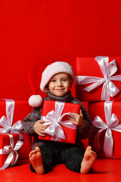 Usmívající se dítě v Santa červené čepici drží vánoční dárek v ruce. Vánoční koncept. — Stock fotografie
