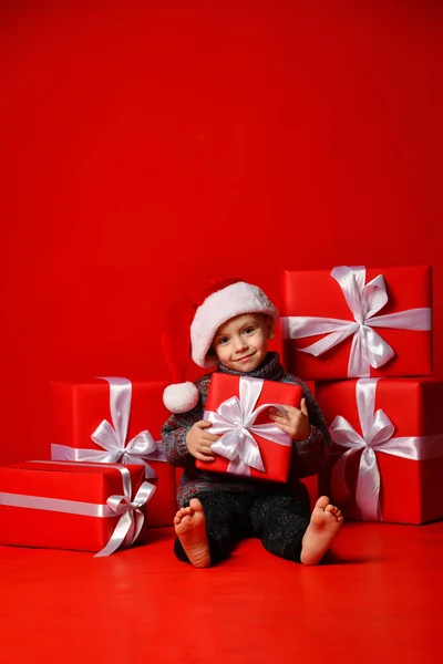 Usmívající se dítě v Santa červené čepici drží vánoční dárek v ruce. Vánoční koncept. — Stock fotografie