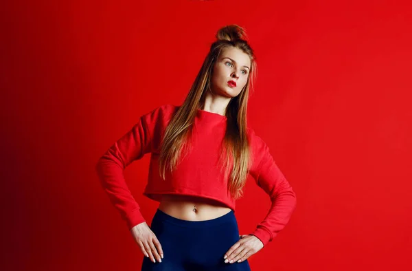 Mujer fitness en ropa deportiva de pie con las manos en las caderas aisladas sobre fondo rojo —  Fotos de Stock